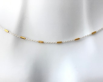 Pode incluir: Um colar de corrente de prata com detalhes de barra dourada.