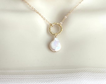 May include: A delicate gold chain necklace with a textured gold circle pendant and a single white baroque pearl hanging from the circle.