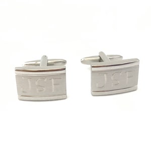 May include: Silver cufflinks with a rectangular design and the initials "JSF" engraved on the front.