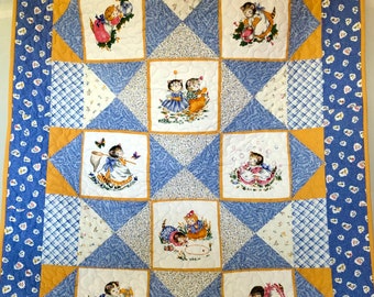 May include: A blue and yellow quilt with a patchwork design featuring kittens playing. The quilt has a white background with blue and yellow squares and a border of blue with white polka dots.