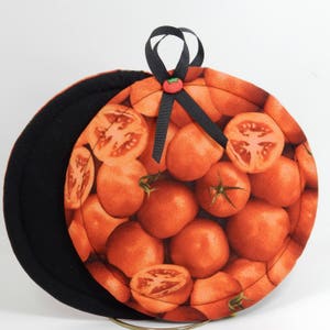 May include: Two round, black and orange fabric pot holders with a black ribbon and a red button. The pot holders are decorated with a pattern of red tomato slices.