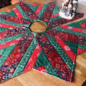 May include: A green and red patchwork Christmas tree skirt with a starburst design. The skirt is made of various fabrics with floral and geometric patterns.