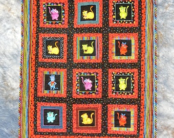 May include: A colorful quilt with a black background and a repeating pattern of cats in various poses. The quilt is framed with a multi-colored striped border.