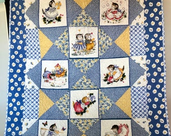 May include: A blue and white quilt with a yellow diamond pattern. The quilt features a variety of scenes with kittens in different activities, including playing with yarn, fishing, and reading a book.
