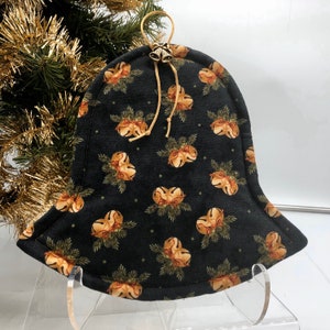 May include: A black fabric Christmas tree skirt with a bell shape and a gold trim. The skirt is decorated with a pattern of gold bells and green pine branches.