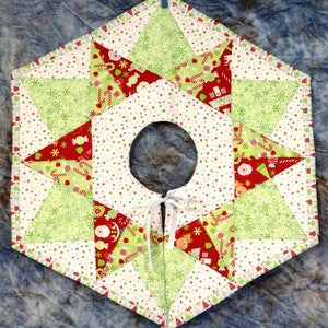 May include: A white, red, and green patchwork Christmas tree skirt with a star design. The skirt has a white ribbon tied in a bow at the center.