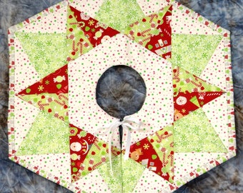 May include: A white, red, and green patchwork Christmas tree skirt with a star design. The skirt has a white ribbon tied in a bow at the center.