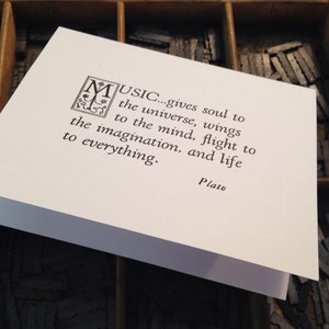 May include: A white card with a black and white quote about music by Plato. The quote reads "MUSIC... gives soul to the universe, wings to the mind, flight to the imagination, and life to everything."
