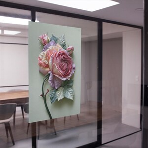 May include: A floral artwork featuring a large, detailed rose in shades of pink, peach, and lavender, with green leaves and a thorny stem. The artwork is mounted on a light green background, creating a three-dimensional effect.