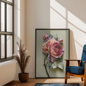 May include: A framed floral art print featuring a large, detailed rose in shades of pink, lavender, and cream. The artwork is set against a soft green background, with a black frame. The image is displayed in a well-lit room with a blue chair and a decorative rug.