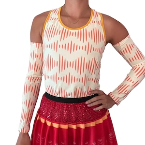 Puede incluir: Un top blanco sin mangas con rayas naranjas y amarillas y brazaletes a juego. El top tiene un escote redondo y los brazaletes son de manga larga. La modelo lleva una falda roja con ribetes dorados y lentejuelas.