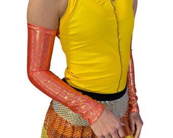 Puede incluir: Una camiseta sin mangas amarilla con un detalle de cadena plateada en la parte delantera se combina con mangas de brazo de lentejuelas naranjas. El atuendo incluye una falda de lentejuelas con capas de plata, naranja y amarillo.