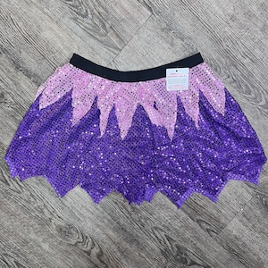 May include: A purple and pink sequined skirt with a jagged hemline. The skirt has a black waistband and a small tag attached to the waistband.