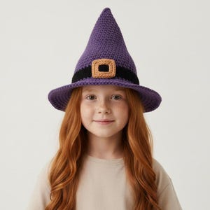 May include: A purple crocheted witch hat featuring a black band around the base and a tan square buckle detail at the front. The hat has a pointed crown and a wide brim, constructed with a visible yarn texture throughout the entire piece.