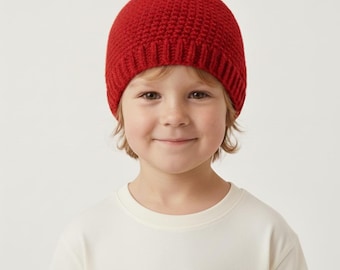 May include: A bright red crochet beanie hat featuring a small brown stem and a single green leaf attached to the top. The hat is constructed with a textured stitch pattern and has a ribbed brim that fits snugly around the head.