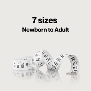May include: A white flexible measuring tape with black numerical markings ranging from 107 to 150. The text 7 sizes Newborn to Adult is printed in black above the tape. The tape is coiled and rests on a reflective surface.
