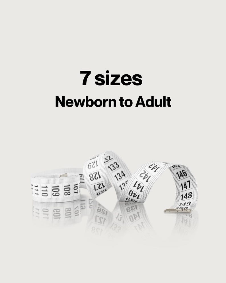 May include: A white flexible measuring tape with black numerical markings ranging from 107 to 150. The text 7 sizes Newborn to Adult is printed in black above the tape. The tape is coiled and rests on a reflective surface.