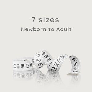 May include: A white measuring tape with black markings is coiled on a light background. The tape is labeled with numbers and the text "7 sizes Newborn to Adult". The tape is used for measuring.