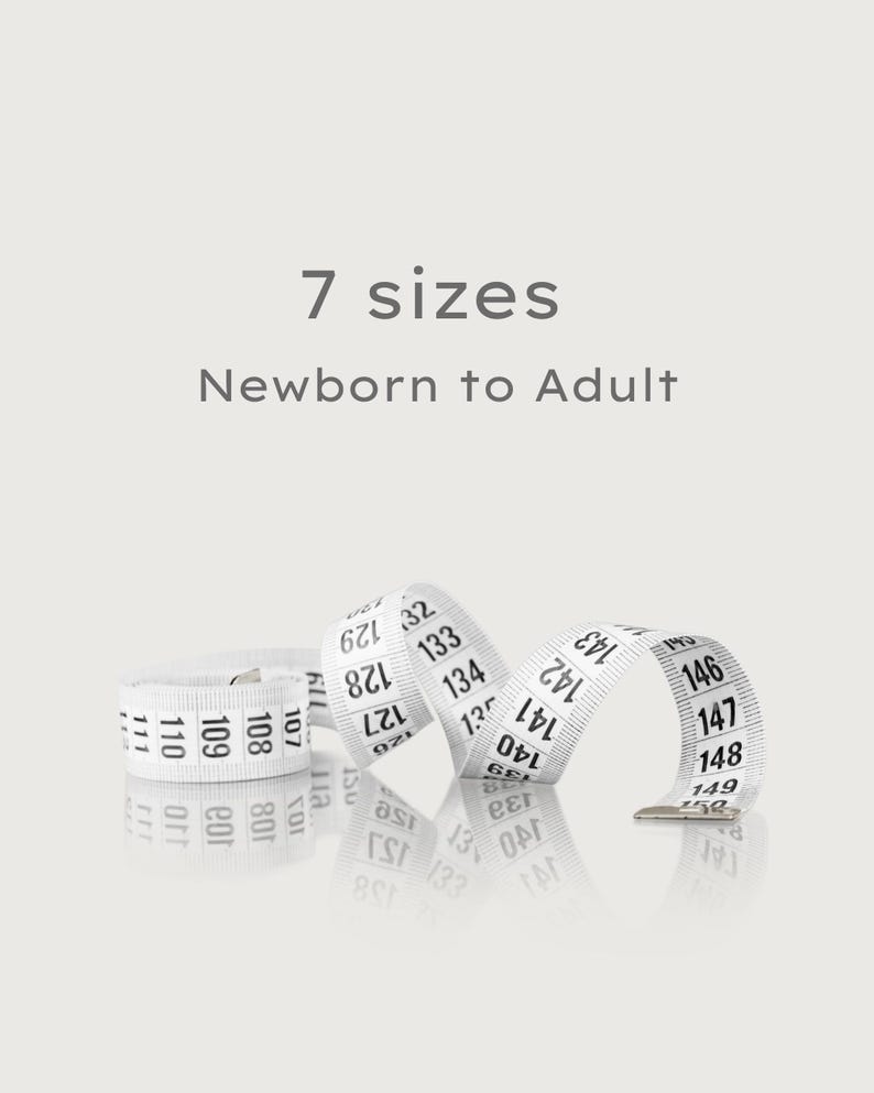 May include: A white measuring tape with black markings is coiled on a light background. The tape is labeled with numbers and the text "7 sizes Newborn to Adult". The tape is used for measuring.