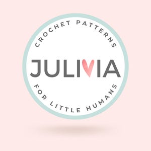 Peut inclure: Logo circulaire avec l'inscription "CROCHET PATTERNS" et "FOR LITTLE HUMANS" dans un cercle bleu clair. Le mot "JULIVIA" est au centre, avec un c&oelig;ur aquarelle rempla&ccedil;ant la lettre "I". Fond rose clair.