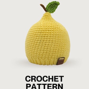 May include: A yellow crochet hat shaped like a pear with a brown stem and a green leaf on top. The hat features a textured stitch pattern and a small brown rectangular tag with the text JULIVIA attached to the bottom edge. The text CROCHET PATTERN is below.