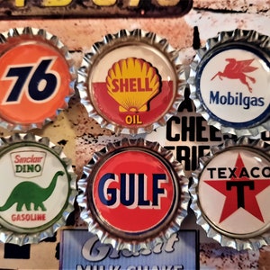 May include: Six vintage-style bottle caps featuring classic oil and gas brand logos. The caps include logos for 76, Shell Oil, Mobilgas, Sinclair Dino Gasoline, Gulf, and Texaco, with a variety of colors and designs.