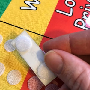 Pu&ograve; includere: Un foglio di punti adesivi bianchi con un supporto bianco. I punti sono disposti in fila e vengono staccati dal foglio. Il foglio &egrave; tenuto da una mano.