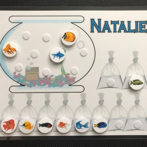 May include: A white card with a fishbowl, a name tag that says "NATALIE", and several bags with fish inside. The fishbowl has a variety of colorful fish, including orange, blue, and green. The bags have a variety of fish, including orange, blue, and green.