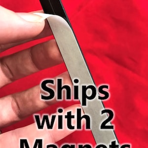 K&ouml;nnte beinhalten: Nahaufnahme einer silbernen Magnetfolie mit Kleber&uuml;ckseite. Die Folie wird abgezogen, um den Kleber freizulegen. Der Text "Ships with 2 Magnets" ist auf dem Bild zu sehen.