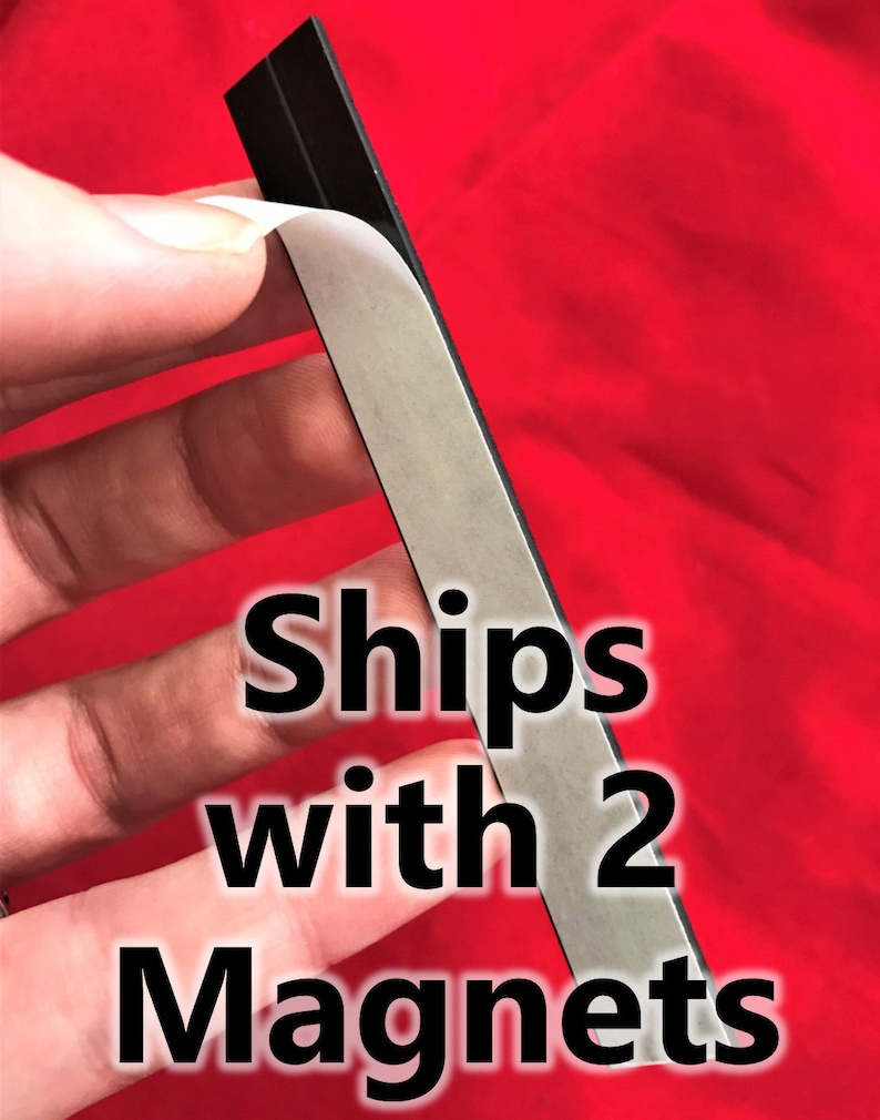 K&ouml;nnte beinhalten: Nahaufnahme einer silbernen Magnetfolie mit Kleber&uuml;ckseite. Die Folie wird abgezogen, um den Kleber freizulegen. Der Text "Ships with 2 Magnets" ist auf dem Bild zu sehen.