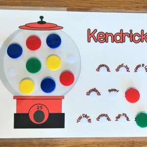 May include: A white gumball machine with a red lid and a black base. The machine has a clear glass globe with colorful gumballs inside. The gumballs are red, blue, green, and yellow. The machine has a number 25 on the front. The name Kendrick is written in red at the top of the image. There are several red and white circles with text around the gumball machine. The text includes "Awesome", "Good Job", "Keep it Up", "Excellent", "Super", "You Did It", "Amazing", "High Five", and "First".