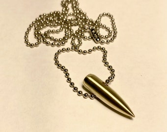 Può includere: Una collana con un ciondolo a forma di proiettile d'argento su una catena a pallini. Il proiettile è lungo circa 5 cm e ha una punta appuntita.