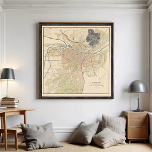 Puede incluir: Un mapa antiguo enmarcado titulado Plano de Lima, que muestra trazados de calles detallados, manzanas urbanas y marcas topográficas en tonos beige, negro y naranja apagado, exhibido como una gran pieza de arte mural cuadrada.