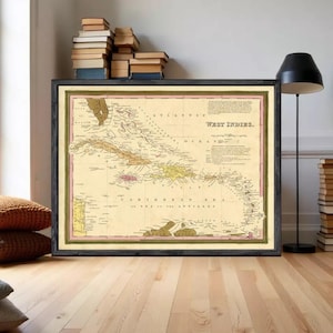 May include: A framed vintage-style map of the West Indies featuring a cream-coloured background with tan landmasses, black text, and a thin pink border. The map displays the Atlantic Ocean, Caribbean Sea, and various islands with detailed labels.