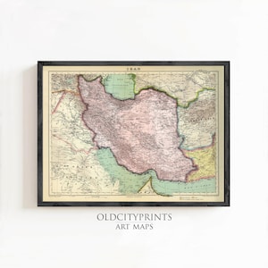 Op de afbeelding: Een ingelijste vintage kaart van Iran, met de grenzen en geografische kenmerken van het land. De kaart is uitgevoerd in roze, groene en gele tinten op een crèmekleurige achtergrond. De lijst is zwart, met de tekst "OLDCITYPRINTS ART MAPS" onderaan.