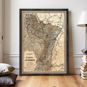May include: A framed vintage map of the Alsace-Lorraine region, featuring intricate details in brown, beige, and blue hues. The map is enclosed in a black frame, adding a classic touch to the artwork. The text "WANDKARTE" and "ELSAß-LOTHRINGEN" are visible.