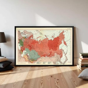 May include: A framed vintage map of the USSR featuring a cream-colored background with landmasses shaded in various tones of red, green, and yellow. The map includes detailed geographical markings, latitude lines, and text labels across the region.