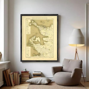 Peut inclure: Une impression de carte vintage encadrée dans un cadre. La carte, aux tons beige et marron, est présentée dans un cadre noir. La pièce présente une palette de couleurs neutres avec un fauteuil beige, un lampadaire et une pile de livres.