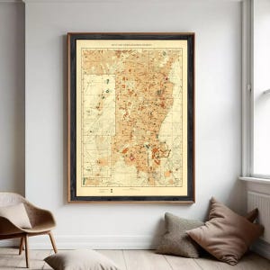 Może przedstawiać: Oprawiona zabytkowa mapa zatytułowana Map of Cairo Showing Mohammedan Monuments, przedstawiająca szczegółową beżowo-brązową kartografię z liniami siatki, układami ulic i oznaczeniami miejsc historycznych, w ciemnej drewnianej ramie.
