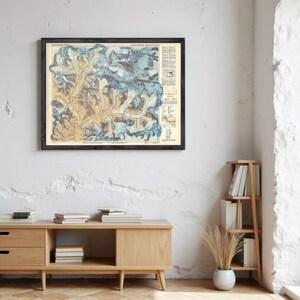 a framed map of the Rocky Mountains hanging on a wall, with a wooden cabinet below it and a bookshelf to the right.