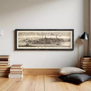 May include: A framed black and white print of a city, possibly a historical map or illustration. The print features detailed architectural elements, including buildings and towers, and is mounted in a dark wooden frame. The text "RIGA METROPOLIS LIVONIA" is visible.