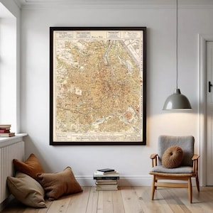 May include: Framed vintage map of a city, featuring detailed streets, buildings, and geographical features. The map is in shades of beige, brown, and red, with text in the upper corners. The frame is dark brown.