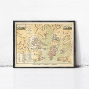 May include: A framed vintage map titled Plan of Valetta and its Harbours, featuring detailed topographical illustrations of the city, fortifications, and surrounding water in muted beige, green, and red tones, with a reference key included.