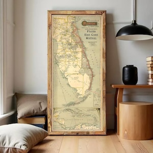Op de afbeelding: Een ingelijste vintage kaart van Florida, met de Florida East Coast Railway. De kaart zit in een houten lijst en heeft een gedetailleerde, verouderde uitstraling met een kleurenpalet van beige, groen en rood. De kaart bevat tekst en geografische details.