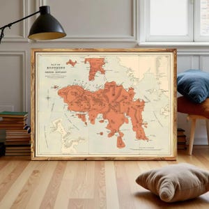 Peut inclure: Carte vintage encadrée de Hong Kong et de Kowloon britannique dans un cadre en bois. La carte présente une illustration détaillée en nuances d'orange et de beige, avec du texte en haut. La carte est posée sur un sol en bois.