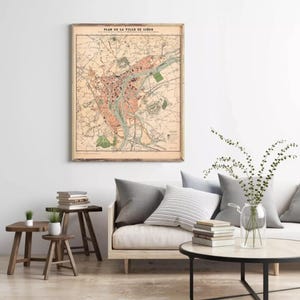 a living room with a large framed map of Paris hanging on the wall, a wooden coffee table with books and a vase of greenery, and a sofa with pillows.