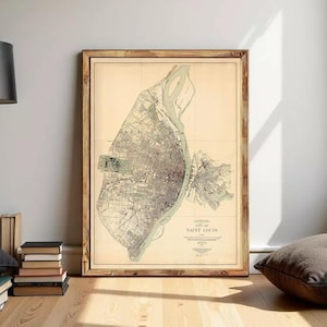 May include: A framed vintage map of the City of Saint Louis printed on a light beige background. The map features detailed black line work showing city streets, blocks, and the Mississippi River. The text reads City of Saint Louis.
