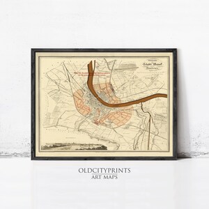 May include: A framed historical map of Basel, Switzerland, featuring a beige background with a prominent brown river winding through the center. The map includes detailed street layouts, highlighted orange districts, and German text labels.