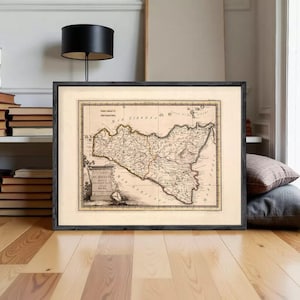 Puede incluir: Mapa antiguo enmarcado de Sicilia, Italia, con cartografía y texto detallados. El mapa está en un marco negro, expuesto sobre un suelo de madera. Los colores del mapa son apagados, con un fondo beige y líneas marrones.