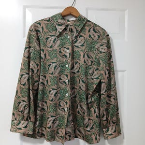 May include: A long-sleeved button-down shirt with a paisley pattern in shades of green, brown, and white. The shirt has a pointed collar and buttoned cuffs. The shirt is hanging on a wooden hanger against a white door.